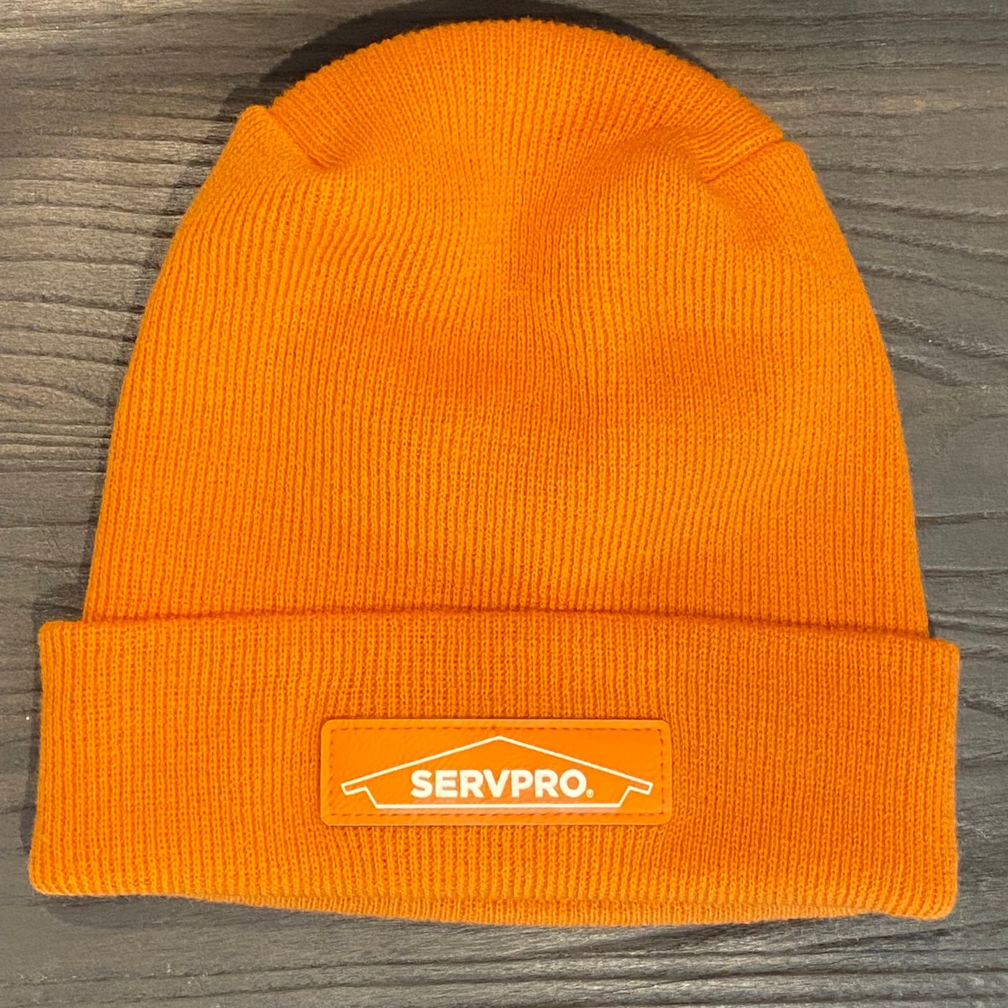 Orange knit beanie with a SERVPRO patch on a wooden surface