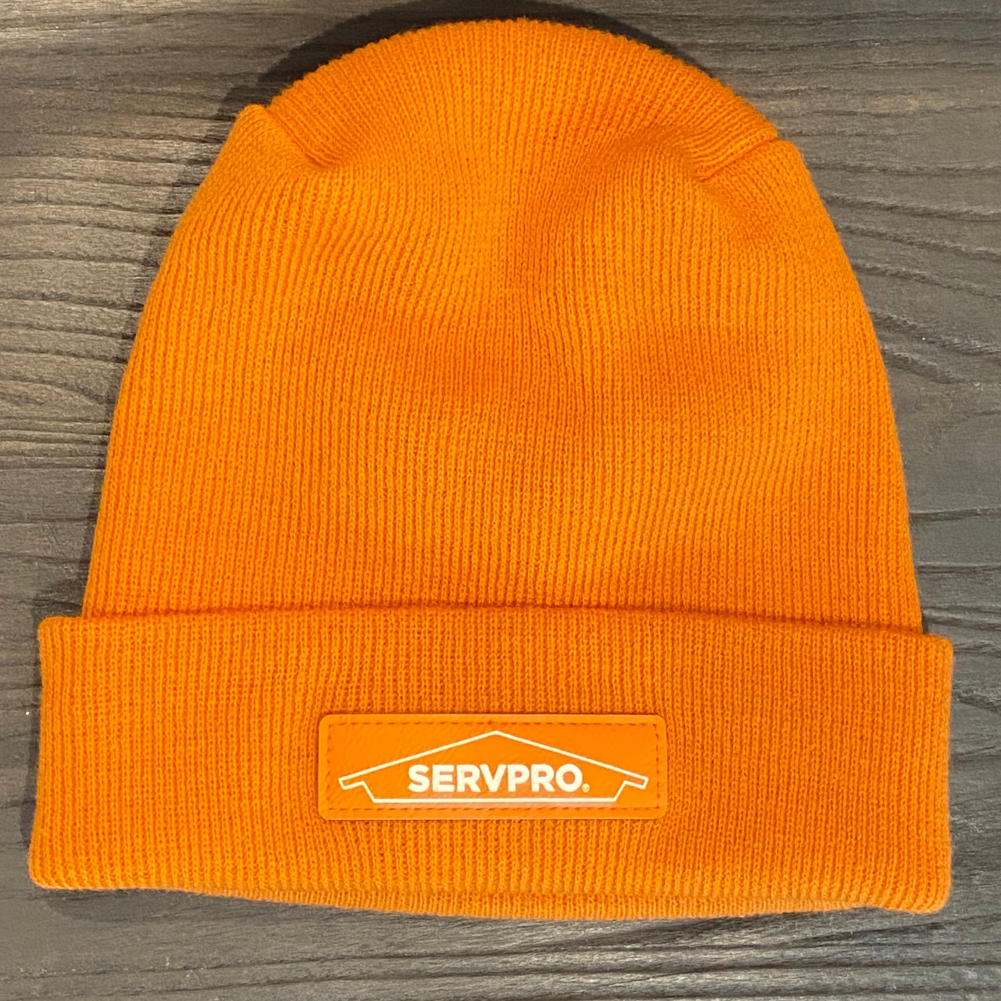 Orange knit beanie with a SERVPRO patch on a wooden surface